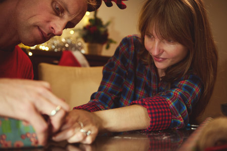A couple and a friend share a warm Christmas moment while wrapping gifts at home, with soft lights and festive decor, conveying family, joy, and togetherness.の写真素材