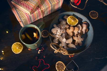 A festive winter scene featuring a plate of sugar-dusted star cookies, a mug of tea, lemon slices, and a patterned gift box-evoking warm, cozy holiday moments.の写真素材