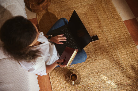 A relaxed home workspace with a person typing on a laptop, jotting in a notebook, and a cup of...