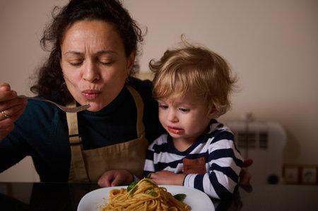 A mother and young child share a pasta meal at a kitchen counter, highlighting family bonding, warmth, and everyday domestic life.の写真素材