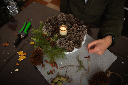 A cozy home scene of a family crafting Christmas decorations on a table, featuring pinecones, greenery, dried citrus, and a glowing candle centerpiece.の写真素材