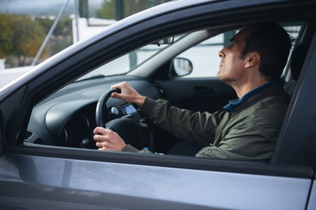 A man sits in the driver s seat, focused on the road with both hands on the steering wheel, captured from the side inside a modern car.の写真素材