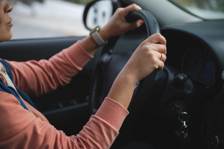 A close-up of a driver gripping the steering wheel inside a car, highlighting focus, safety, and everyday travel. Ideal for commuting, road trips, or family journeys.の写真素材