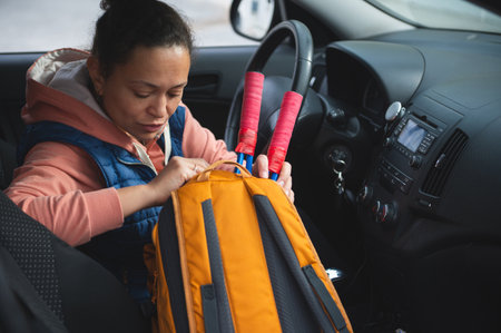 A woman sits inside a car, packing an orange backpack with pink straps, preparing for a trip or...