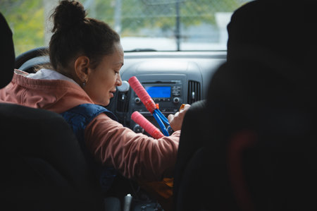 A young girl sits in the car's front seat, smiling and playing with bright party poppers near the dashboard, capturing a cheerful moment during family travel.の写真素材