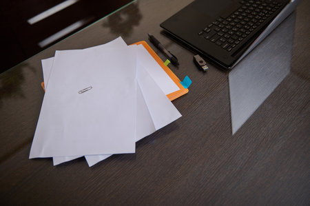 A clean desk with scattered documents, a laptop, USB drive, and colorful sticky tabs, capturing a...