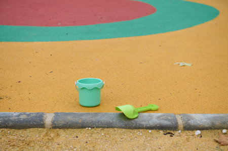 Bright green sand bucket and matching shovel sit on a yellow playground surface, with colorful circles in the background, evoking outdoor play, kids, and family fun.の写真素材