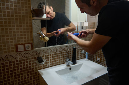 A focused man at home cleans a blue cloth by the sink in a modern bathroom, capturing balance between family life and entrepreneurial work.の写真素材