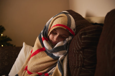 A warm, intimate scene of a child tucked in a thick patterned blanket on a sofa, enjoying a peaceful...