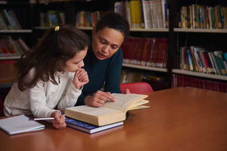 A mother and daughter study together at a library table, turning pages and sharing ideas. The scene...