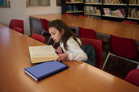 A young student reads a book at a library table, with a backpack nearby. Calm, focused learning...