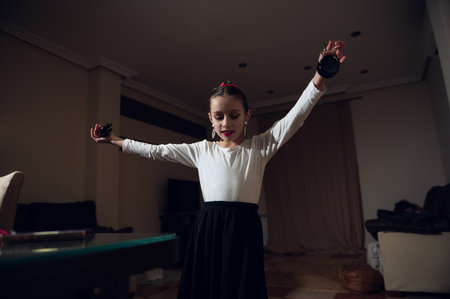 A young girl performs a graceful dance with arms extended indoors, wearing a white top and black skirt. The scene conveys joy, practice, and home creativity.の写真素材