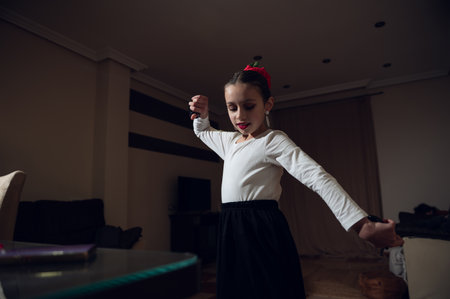 A young girl dances gracefully indoors in a white top and black skirt, with a red hair accessory. She spins with arms extended, capturing movement and focus.の写真素材