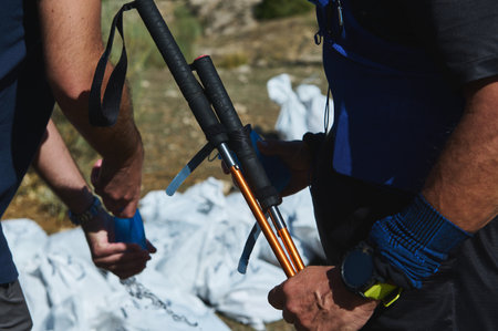 Two hikers prepare gear in a sunny outdoor setting, grabbing trekking poles and packing bags for a...