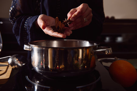 A woman in a dark outfit sprinkles spices over a shiny pot on a stove, with an orange nearby, evoking cozy winter cooking and holiday warmth.の写真素材