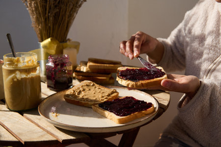 A cozy morning scene shows toast being prepared with peanut butter and jam, captured with warm light...