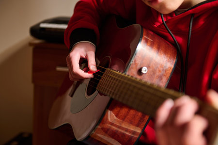 A teen plays an acoustic guitar in a cozy indoor setting, concentrating on strings and fingers,...