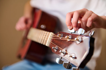 Close-up of a person tuning an acoustic guitar, focusing on the hand adjusting tuning pegs and...