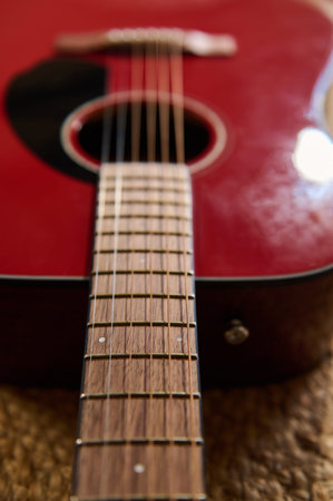 Close-up of a red acoustic guitar neck and fretboard with strings and sound hole, evoking musical...