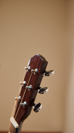 Close-up of an acoustic guitar headstock showing tuning pegs, strings and wood grain against a soft...