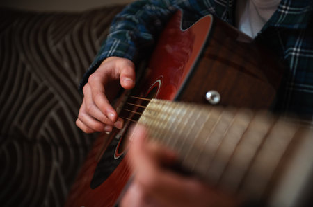 Teenage boy casually strumming an acoustic guitar at home, creating a relaxed, cozy atmosphere while...