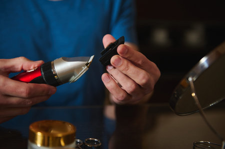 Close-up of hands changing a clipper blade on an electric trimmer for at-home grooming and haircut...