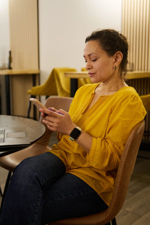 Female entrepreneur and digital nomad sits in a cafe, checking her smartphone while telecommuting...