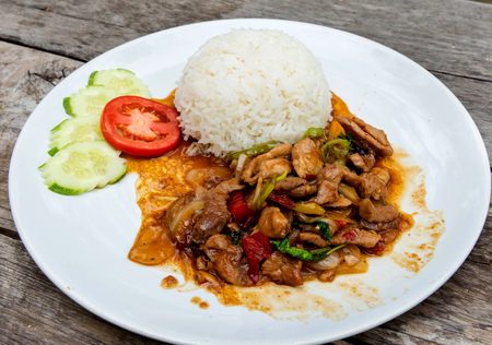 fried pork with chilli ,basil,cucumber ,tomato sliced neat rice on white plate.の写真素材