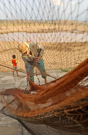A fisherman fixes his net near a drought stricken dam in Madiun, East Java Indonesia, on August 28th, 2003. The long drought season in Indonesia this year has left thousands suffering from access to water.のeditorial素材
