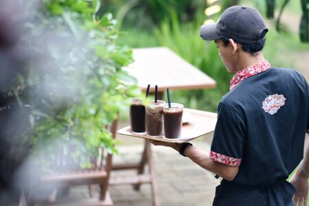 The waiter delivers a drink at the Classic Chocolate Cafe with a green atmosphere with a private...