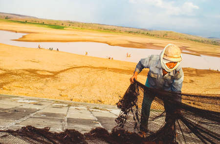 A fisherman fixes his net near a drought stricken dam in Madiun, East Java Indonesia, on August 28th, 2003.のeditorial素材