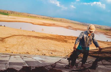 A fisherman fixes his net near a drought stricken dam in Madiun, East Java Indonesia, on August 28th, 2003.のeditorial素材