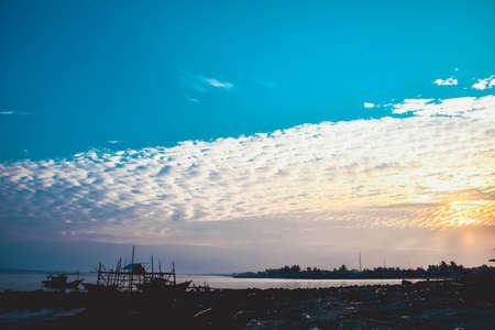 A beautiful shot of a bright yellow sun rising among the silhouettes of a fishing boat on the beach...