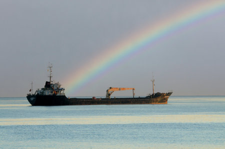 Cargo ship in the sea with rainbow on the sky background.