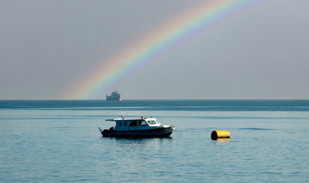 Boat in the sea with a rainbow in the background and a shipの写真素材