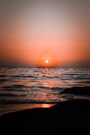 Vibrant sunset descending on the horizon, sea in golden colors, small waves gently touching the sands,の写真素材