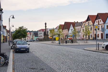 street scene in a small European town. The street is paved with cobblestones, and a central pedestrian island is visible, featuring benches and young trees.の写真素材
