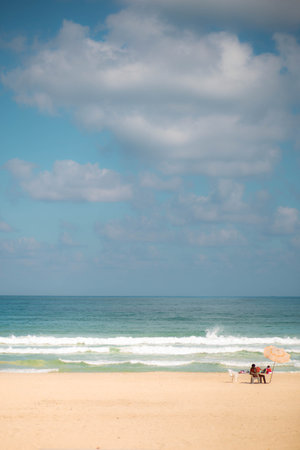 Couple relaxing on the beach under the blue sky and white cloudsの写真素材