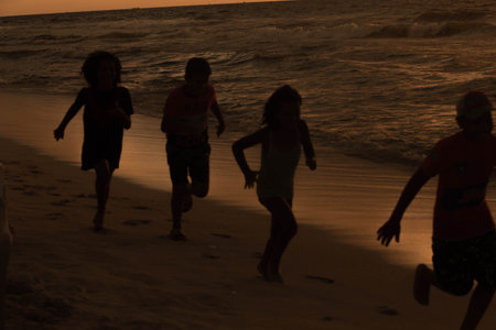 Silhouette of children running on the beach in the evening.の写真素材