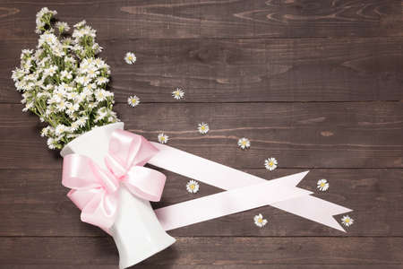 White cutter flowers are in the vase with ribbon on the wooden background.の写真素材
