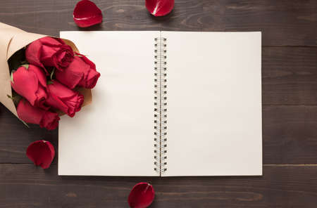 Red roses flower with the notebook are on the wooden background.の写真素材