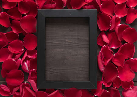 Beautiful red rose petals and frame picture are on the wooden background.