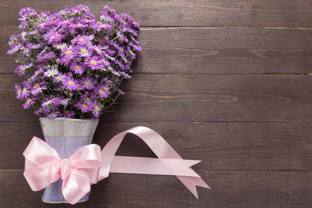 Purple cutter flower of the vase and ribbon are on the wooden background.の写真素材