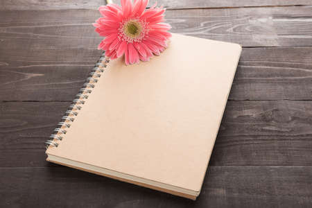 Pink gerbera flower and notebook are on the wooden background.の写真素材