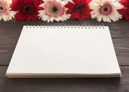 Pink and red gerbera flowers with notebook are in the wooden background.の写真素材