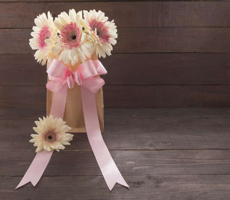 Pink and white gerbera flowers with ribbon are in the bag, on the wooden background.の写真素材
