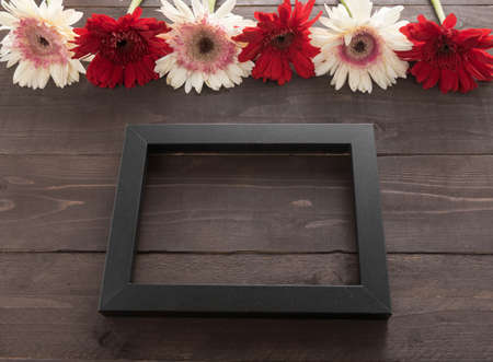 Pink and red gerbera flowers with picture frame are in the wooden background.の写真素材