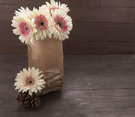 Pink and white gerbera flowers and pine cones are in the bag, on the wooden background.の写真素材