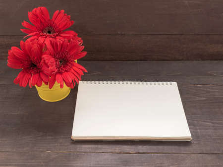 Red gerbera flowers are in the flowerpot, on the wooden background with card.の写真素材