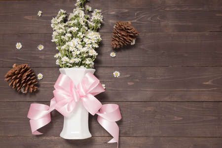 White cutter flowers are in the vase with ribbon on the wooden background and pine cones.の写真素材